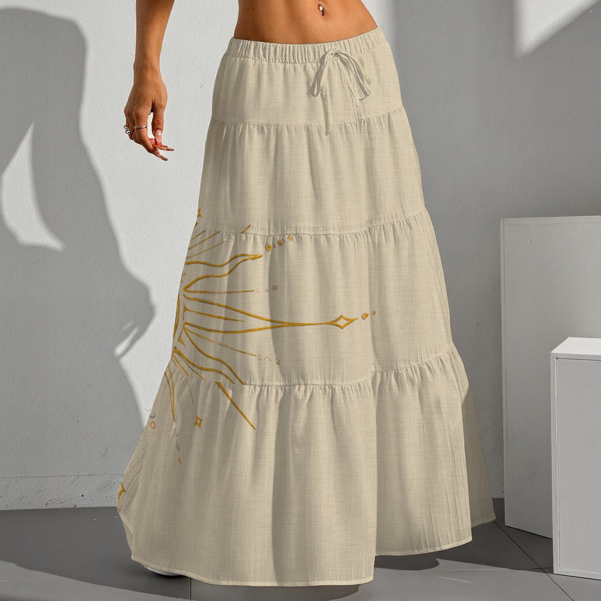 Front view of cream tiered maxi skirt with drawstring waist and golden sun graphic.