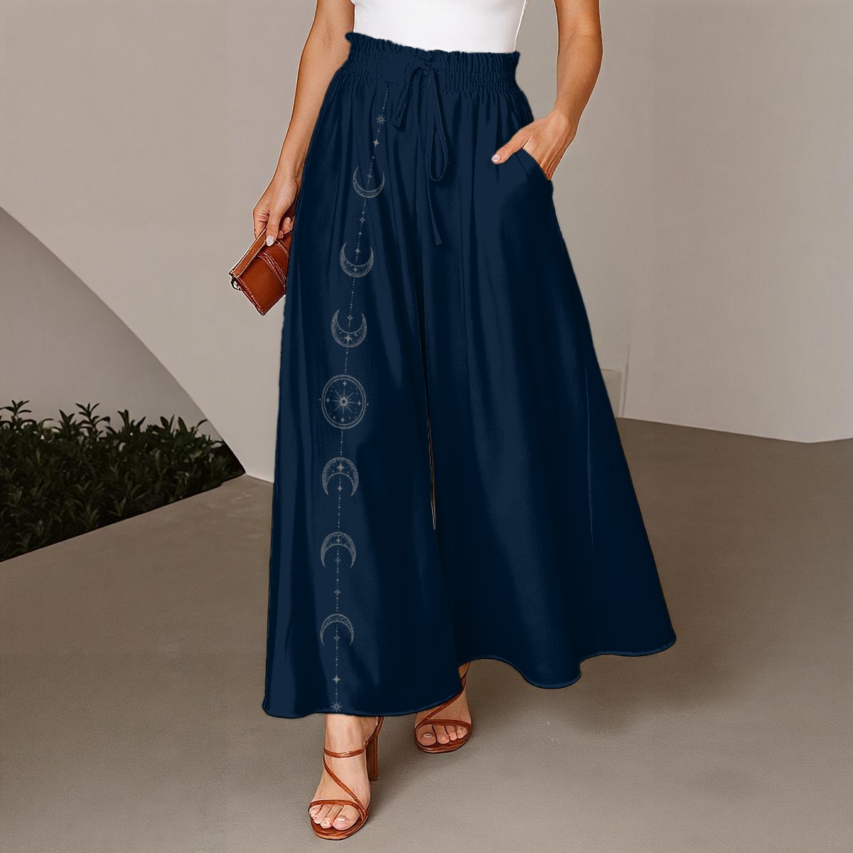 Front view of navy wide-leg pants with a smocked drawstring waist and moon phase print on one leg