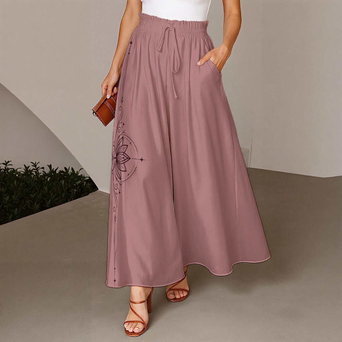 Front view of dusty rose wide-leg pants with a smocked drawstring waist and lotus graphic on the left leg