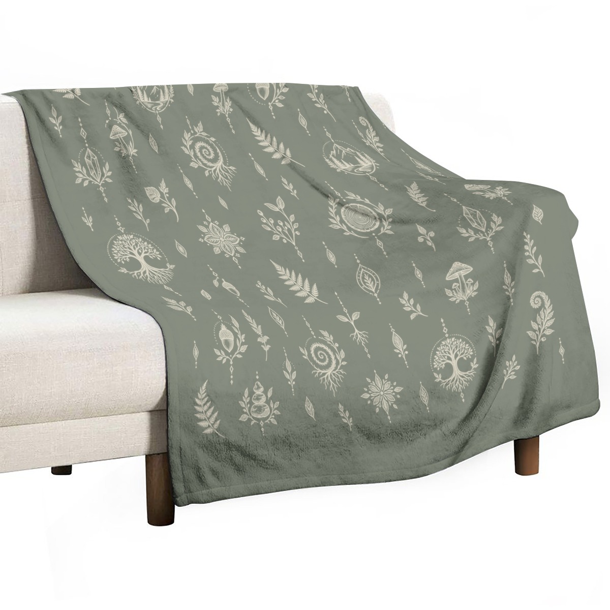 Sage green blanket draped over a light sofa with white botanical and nature motifs