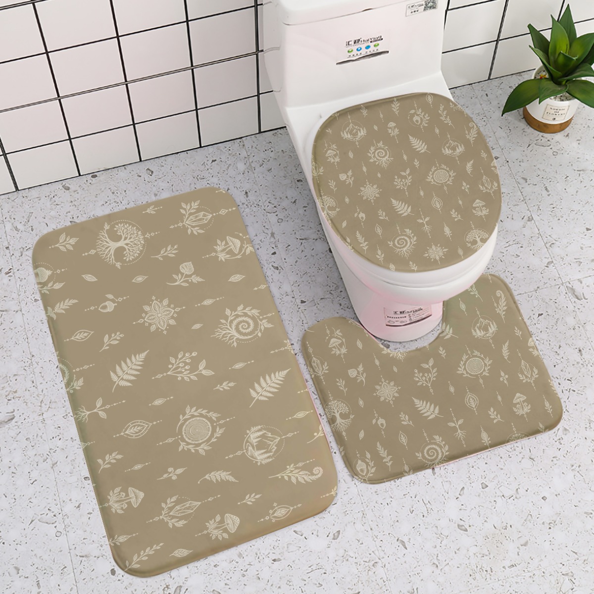 Three-piece beige bath mat set with white botanical and nature motifs arranged around a toilet